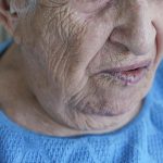 Rosto de idosa com blusa azul para ilustrar conteúdo sobre paralisia facial.